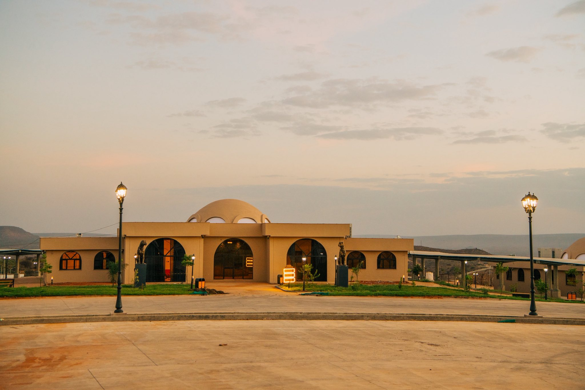 The cultural pavilion and meeting halls at dusk, leopards flanking the arched entrance